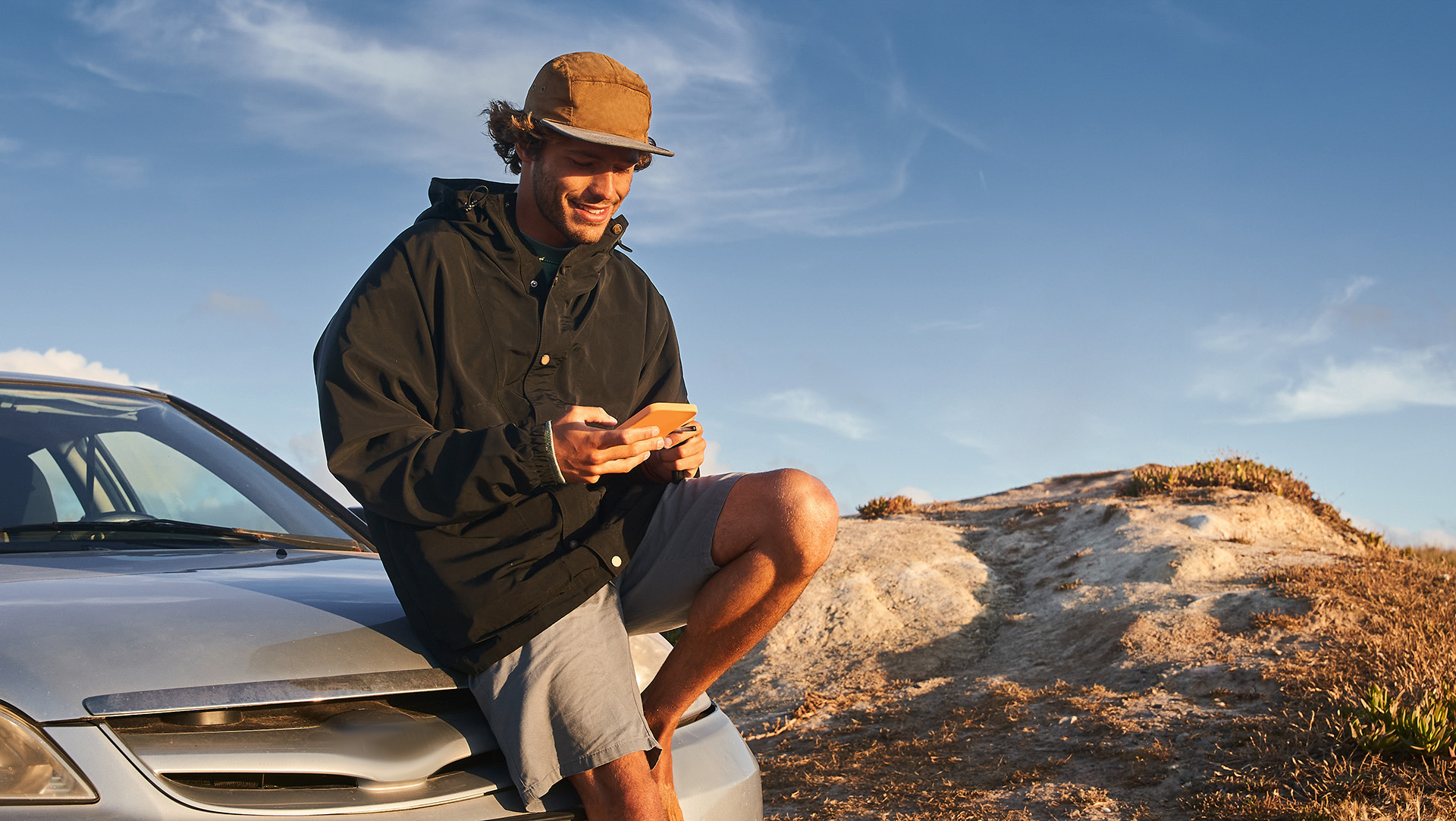 man sitting on car with cell phone